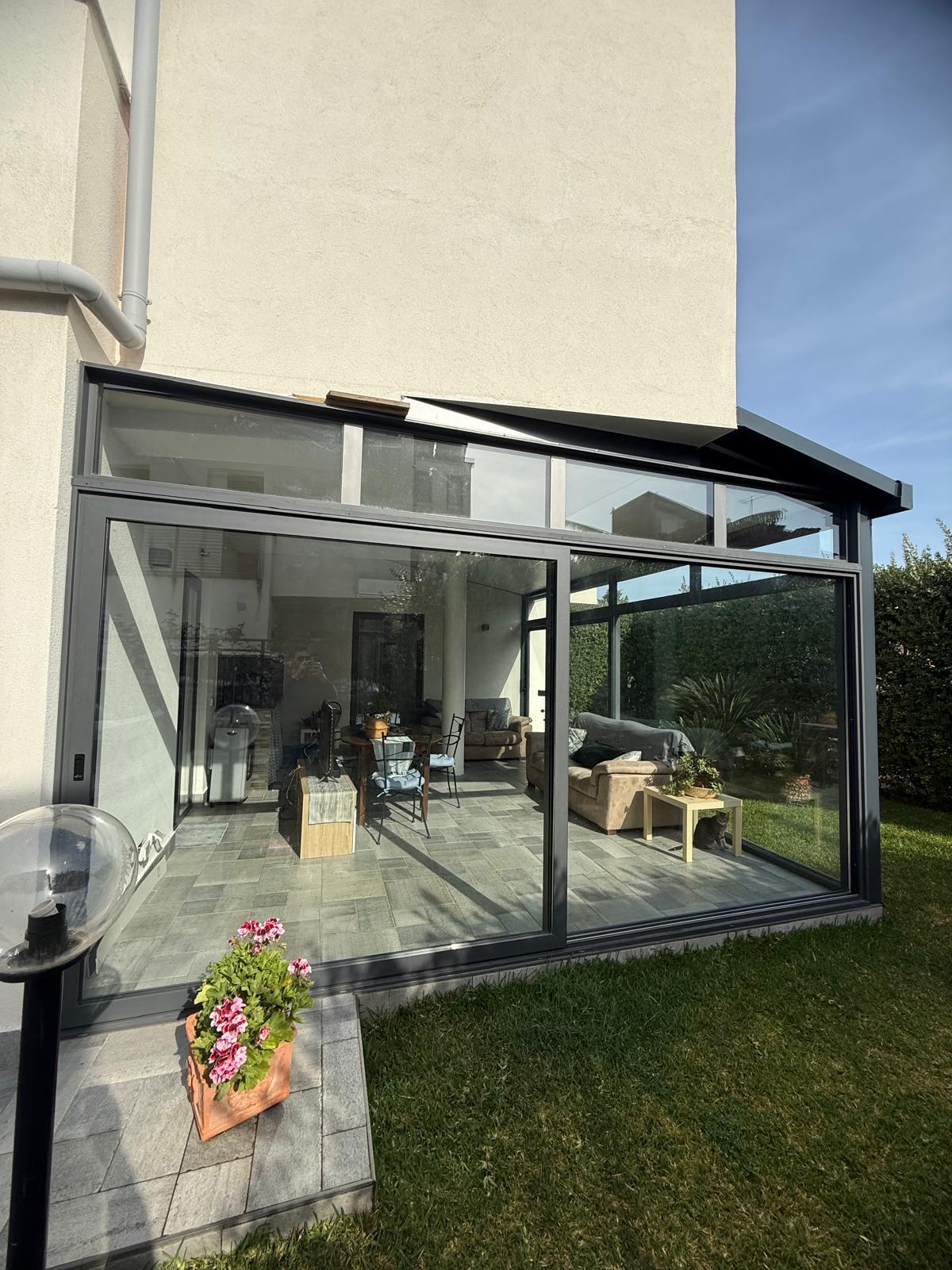 Veranda in alluminio antracite con tetto inclinato e ampie vetrate panoramiche